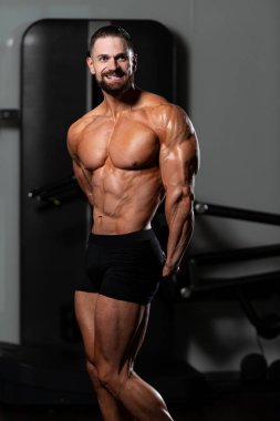 Yakışıklı Genç Adam Spor Salonunda Güçlü Duruyor ve Kaslarını Geriyor - Kas Atletik Vücut Geliştirici Spor Sonrası Spor Pozisyonu