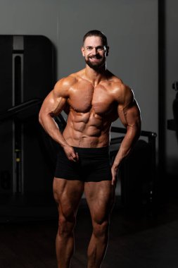 Yakışıklı Genç Adam Spor Salonunda Güçlü Duruyor ve Kaslarını Geriyor - Kas Atletik Vücut Geliştirici Spor Sonrası Spor Pozisyonu