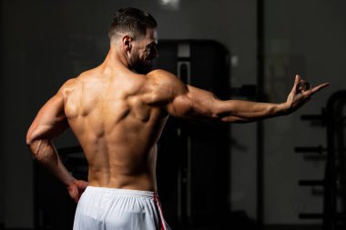 Yakışıklı Genç Adam Spor Salonunda Güçlü Duruyor ve Kaslarını Geriyor - Kas Atletik Vücut Geliştirici Spor Sonrası Spor Pozisyonu