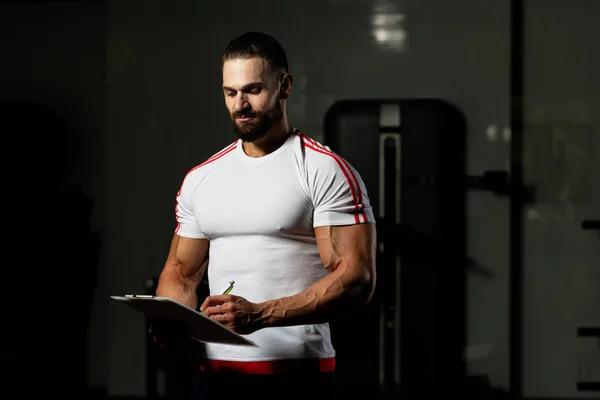 Personal Trainer Takes Notes On Clipboard In Fitness Center Gym