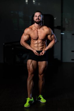 Yakışıklı Genç Adam Spor Salonunda Güçlü Duruyor ve Kaslarını Geriyor - Kas Atletik Vücut Geliştirici Spor Sonrası Spor Pozisyonu