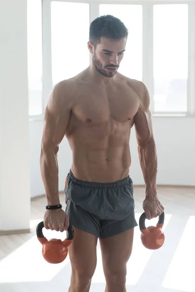 用水壶钟在一个黑暗的健身房 健美锻炼重配壶铃工作的年轻人 — 图库照片