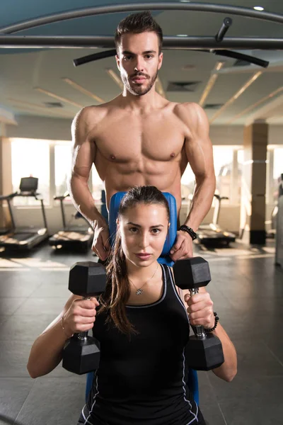私人教练显示年轻女子如何培养与 Dumbbels 在健身房里的肩膀上 — 图库照片