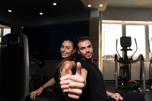 Pretty Good Looking And Attractive Young Couple With Muscular Body Relaxing Or Resting In Gym and showing Thumbs-up close-up