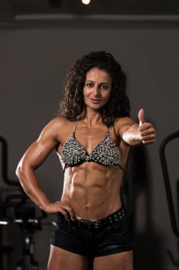 Kaslı kadın ise güçlü bir spor salonunda duran ve kasları - kaslı atletik vücut Fitness Model çalışmaları sonra poz esneme başparmak gösterilmesini