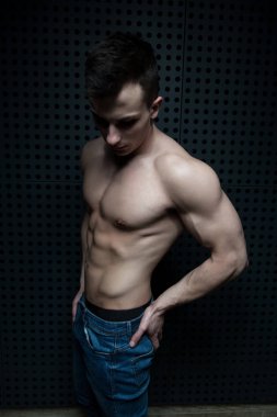 İyi eğitilmiş vücudunu gösteren genç bir adamın portresi mavi kot giyerken - kaslı atletik vücut geliştirici spor modeli pozu duvarın yanındaki duvarda egzersiz yaptıktan sonra - metinleriniz için bir yer