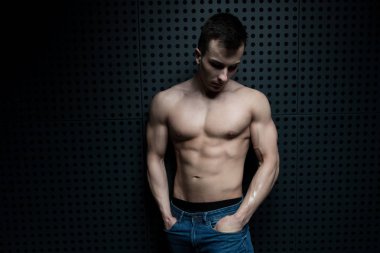 Sağlıklı Genç Adam Duvar 'a Karşı Güçlü Duruyor ve Mavi Kot Giyerken Kaslı Atletik Vücut Geliştirici Spor Pozisyonu - Metinleriniz İçin Bir Yer