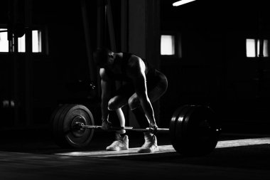 Atlet onun diz ve bar salonunda yakınındaki duruyor ve bir deadlift yapmak hazırlanıyor
