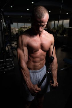 Spor salonundaki adam spor salonunda kablolu TV ile trisepslerini çalıştırıyor.