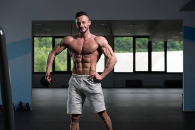 Yakışıklı Genç Adam Spor Salonunda Güçlü Duruyor ve Kaslarını Geriyor - Kas Atletik Vücut Geliştirici Spor Sonrası Spor Pozisyonu