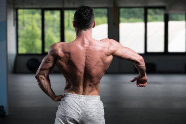 Yakışıklı Genç Adam Spor Salonunda Güçlü Duruyor ve Kaslarını Geriyor - Kas Atletik Vücut Geliştirici Spor Sonrası Spor Pozisyonu