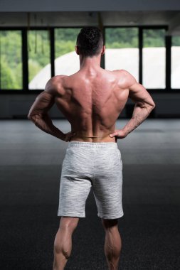 Yakışıklı Genç Adam Spor Salonunda Güçlü Duruyor ve Kaslarını Geriyor - Kas Atletik Vücut Geliştirici Spor Sonrası Spor Pozisyonu