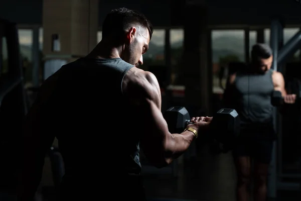 Hombre muscular ejercitando bíceps con mancuerna — Foto de Stock