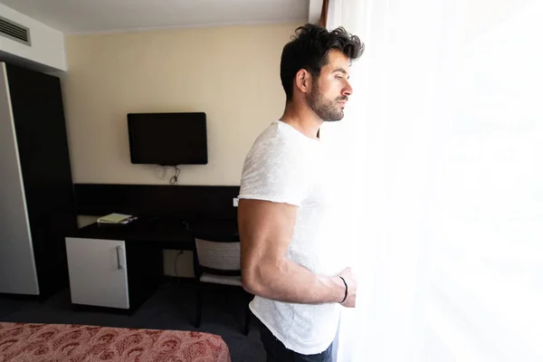 Молодой человек стоит у окна в гостиничном номере — стоковое фото