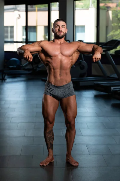 Красивый мускулистый человек, демонстрирующий мышцы в спортзале — стоковое фото