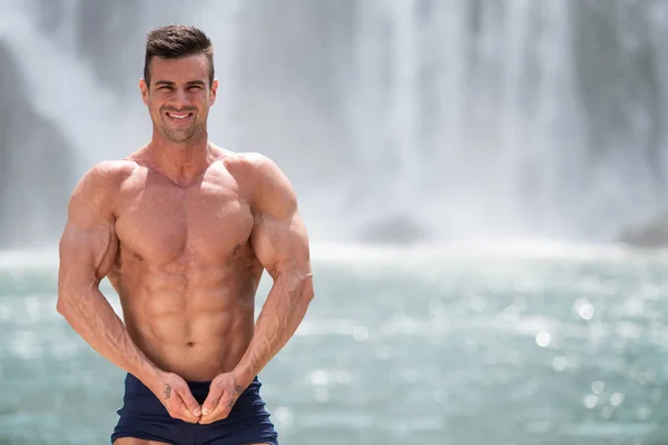 Bodybuilder lässt vor Wasserfall die Muskeln spielen — Stockfoto