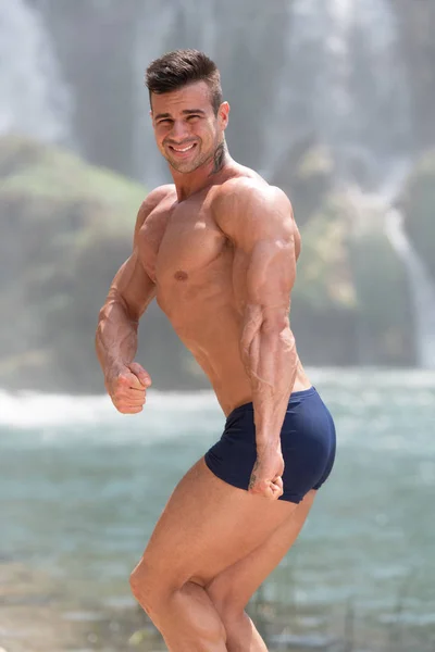 Healthy Man Flexing Muscles in Front of Waterfall — Stock Photo, Image