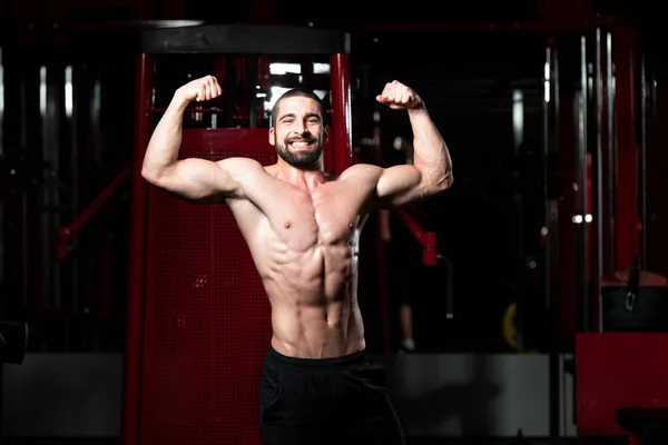 Biceps pose d'un jeune homme dans la salle de gym — Photo