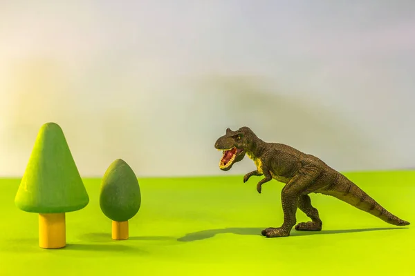 Toy dinosaur in a toy forest. like a real T-rex on a bright studio background with wooden trees. Eco toys.