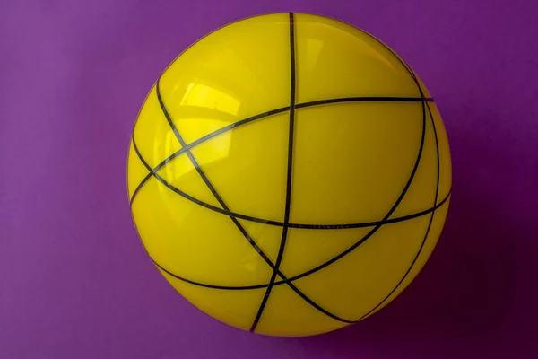 Big yellow glass ball on a violet background. Still life of striped yellow ball on bright violet table.