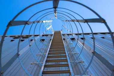 Hangarın çatısına dikey metal merdiven. Koruyucu bir çerçeve ile çevrili merdiven