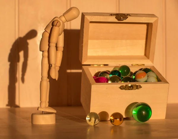 Triste homme en bois devant un coffre avec des boules de verre colorées,. poupée en bois et coffre au trésor . — Photo