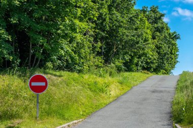 Yol işareti girmeyin. O tarafa giriş yok. Yol yanlış yöne gidiyor. Yeşil ağaçlar ve mavi gökyüzü