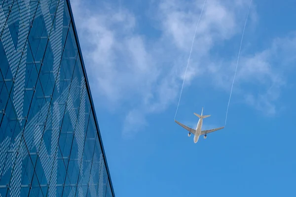 Airplan leaves a trail in the blue sky. Airliner is takking off over the building. White cloud in the blue sky in which the plane flies — Stock Photo, Image