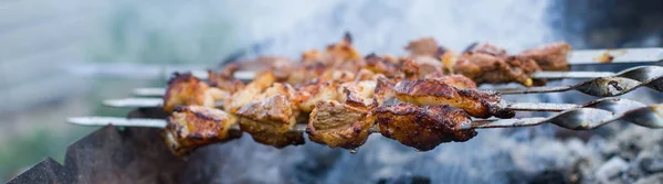 Shashlik or shashlyk preparing on a barbecue grill over charcoal. Grilled cubes of pork meat on metal skewer. Meat on skewers is roasted on fire