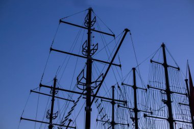 Akşamları mavi gökyüzüne karşı fırkateyn direkleri siluetleri. Gün batımında mast yatı. Karanlıkta bir korsan gemisinin direkleri. Degrade gökyüzü.