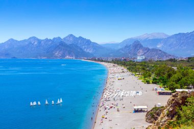 Dağların arka planında şehir plajıpanoramik görünümü. Yelkenli ve pitoresk bir plaj ile mavi deniz. Akdeniz'de Tatil.