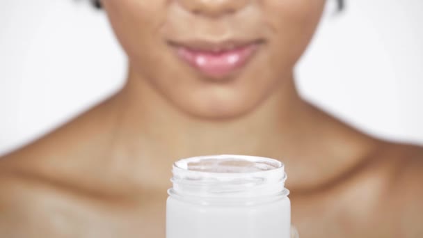 コンテナーと白で隔離を笑顔から化粧品クリームを取っているアフリカ系アメリカ人の女性観をトリミング — ストック動画