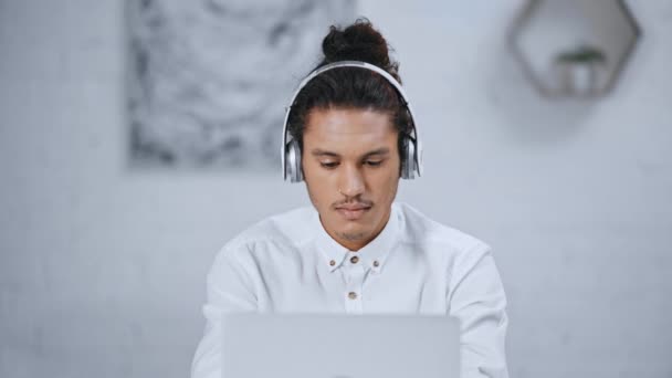 音楽を聴く ノート パソコンとスマート フォンを使用してヘッドフォンでハンサムな実業家 — ストック動画