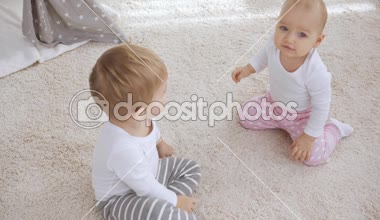 sevimli çocuk halı üzerinde oturan ve kamera parmak ile işaret ederken bebek kız kardeşi tüm fours üzerinde tarama ve sonra eller alkışlayan