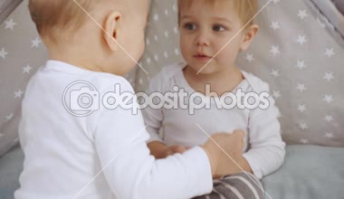 sevimli bebek kamera parmak ile işaret ve sonra bebek Wigwam şaşkın kardeşi ile oynuyor