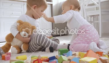 Bebek kız kardeşi yüzüne dokunmadan iken şaşkın ve gülümseyen Toddler çocuk oyuncak ayı ile halı üzerinde oturuyor