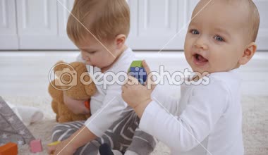 bebek kardeşi ahşap bloklar ile oynarken oyuncak ayı ile halı üzerinde oturan Toddler çocuk, sonra kardeşi yükselen ve oyuncak ile yürüme uzaklaşırken