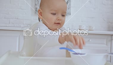 şirin çocuk sandalyesinde oturan, sonra anne onu kaşık ve kase ve bebek plastik yemekler ile oynuyor veren