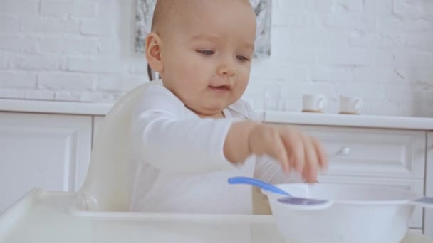 可爱的孩子坐在高脚椅上 然后母亲给她的勺子和碗和婴儿玩塑料盘子 — 图库视频影像