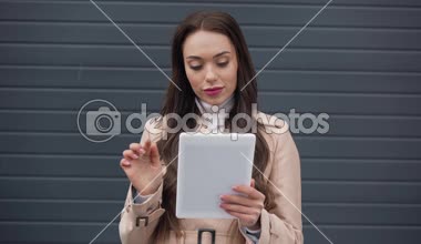 gülümseyen bej trençkot dijital tablet rüzgarlı havalarda kullanma içinde zarif genç kadın