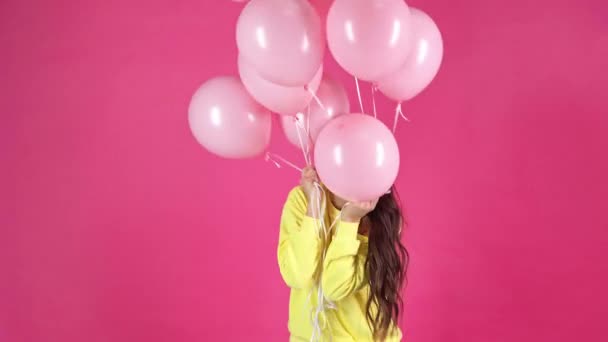 studio shoot of happy young woman holding pink air balloons and turning around on crimson background