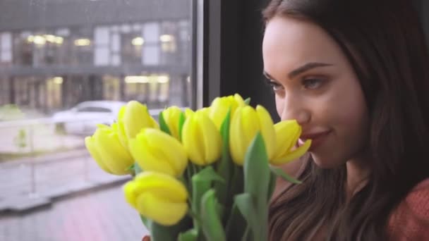 Красивая Молодая Женщина Стоит Окна Нюхает Желтые Тюльпаны Закрытыми Глазами — стоковое видео
