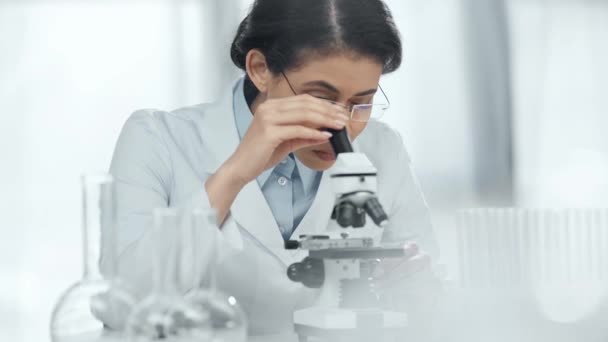 実験室で顕微鏡を通してサンプルを見る眼鏡のアフリカ系アメリカ人科学者の選択的焦点 — ストック動画