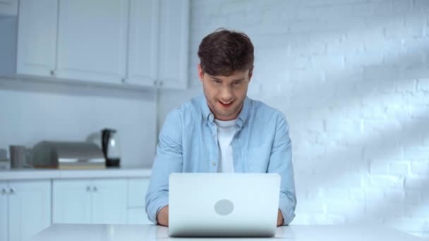兴奋的自由职业者在蓝色衬衫打开笔记本电脑和打字键盘与微笑在厨房 — 图库视频影像
