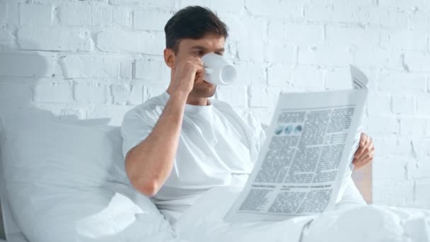 Konzentrierter Mann Weißen Shirt Der Bett Kaffee Trinkt Und Zeitung — Stockvideo