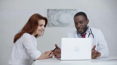 dizüstü bilgisayarın yanında otururken iki çok kültürlü doktor konuşuyor ve gülümsüyor 