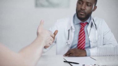 hastanede işyerinde otururken hasta ile el sıkışma affable afro-amerikan doktor
