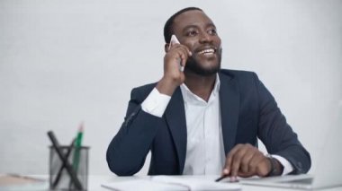 neşeli afro-amerikan işadamı akıllı telefon konuşuyor ve ofiste işyerinde otururken uzağa bakıyor