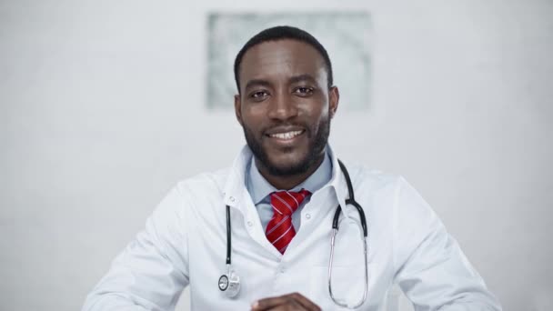 ハンサムな 肯定的なアフリカ系アメリカ人の医者は カメラを見ながら微笑んでいます — ストック動画