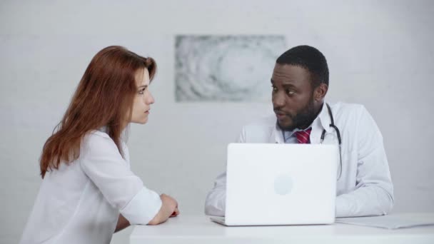 ラップトップの近くに座っている間 深刻なアフリカ系アメリカ人の医者が同僚と話す — ストック動画